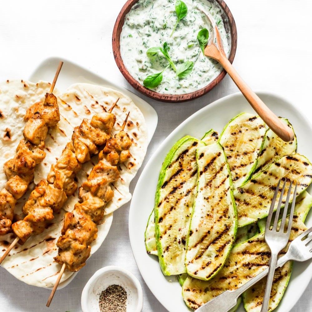 Teller mit gegrilltem Gemüse und Fleischspießen. Fladenbrot, Dip und Gewürzschale. Draufsicht.