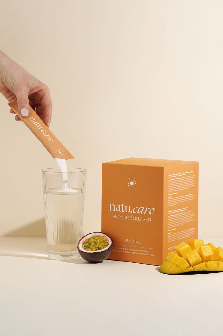 Hand gießt Pulver aus Beutel in Glas. Schachtel, Glas, Mango und Maracuja. Aufschrift "natu.care".