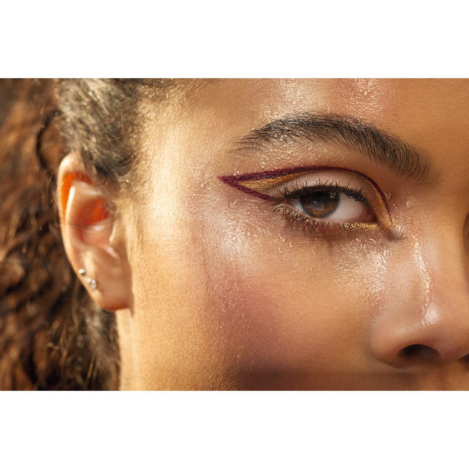 Nahaufnahme eines Auges mit Eyeliner. Goldener und burgunderfarbener Eyeliner-Look, der die Augenform betont.