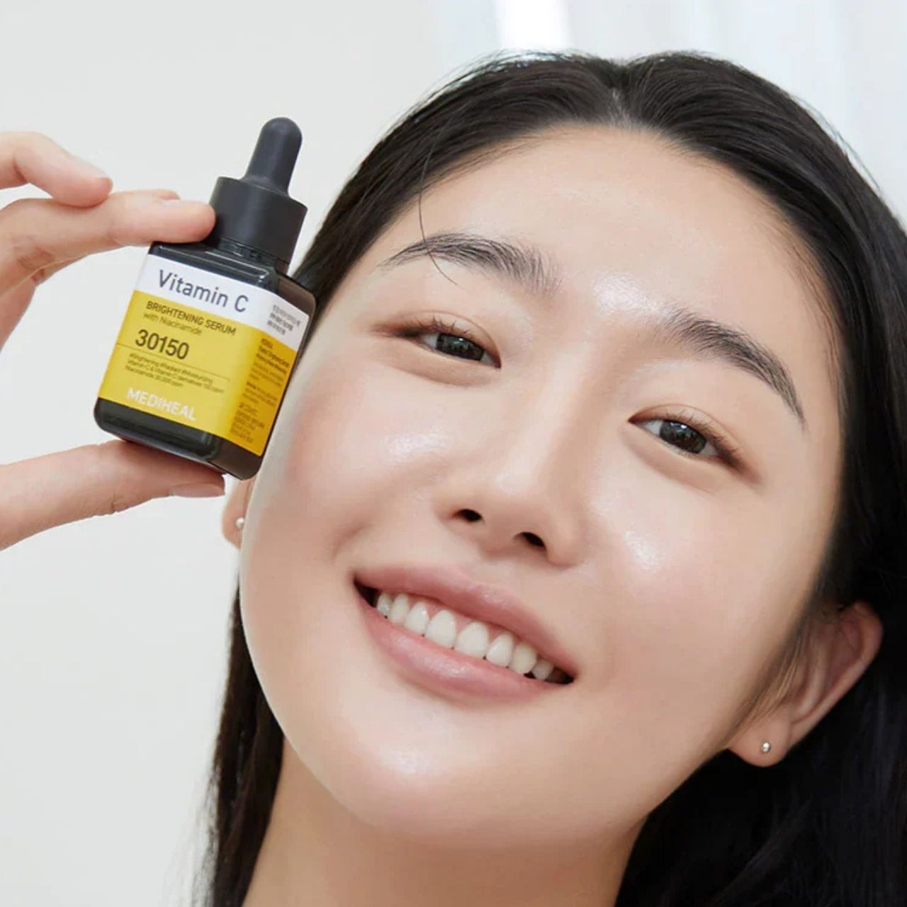 Frau hält eine Flasche Mediheal Vitamin C Serum vor ihr Gesicht. Gelbes Etikett mit Produktbezeichnung.