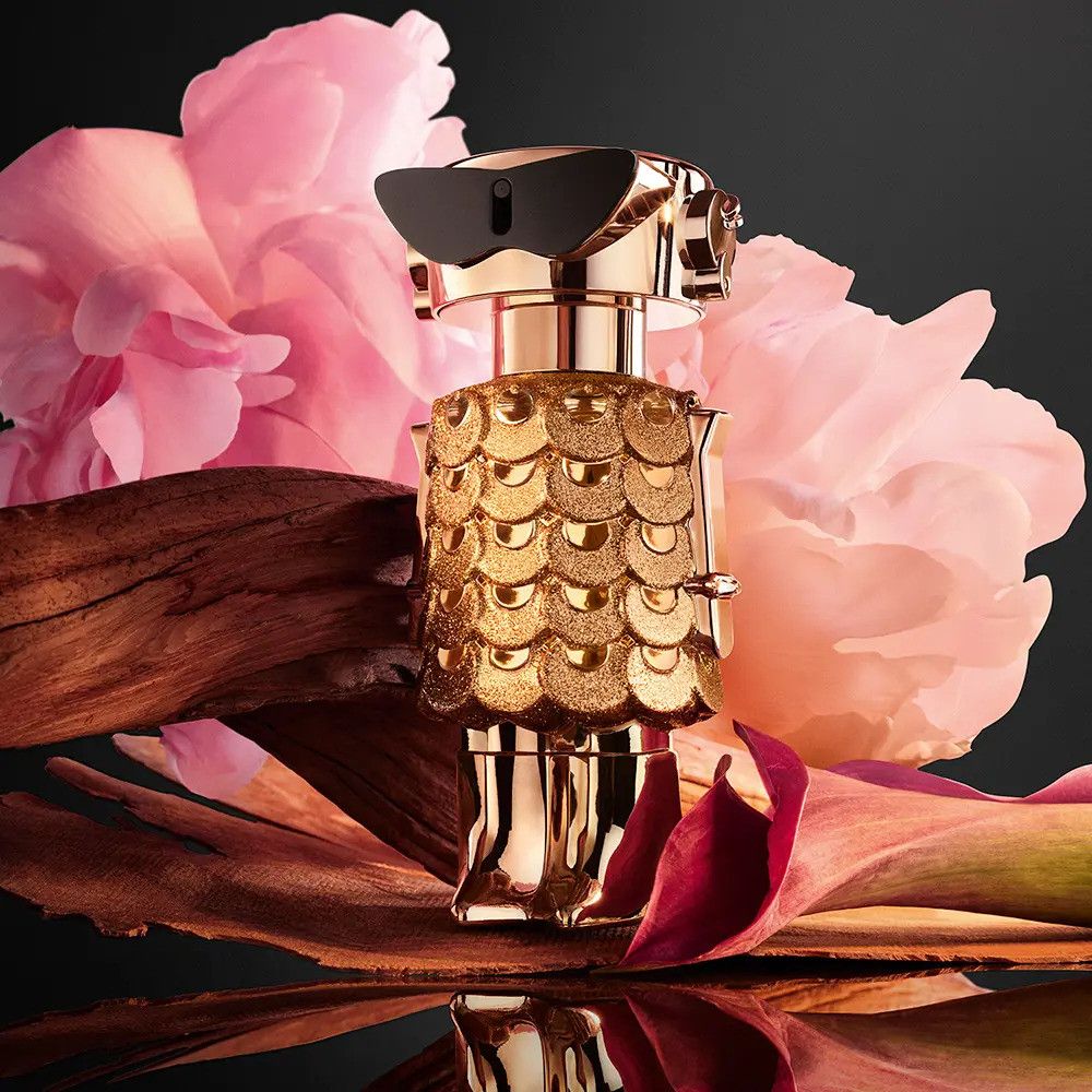 Goldfarbener Flakon mit schwarzer Sonnenbrille, umgeben von Blüten und Holz. Flakon-Design: Roboter.