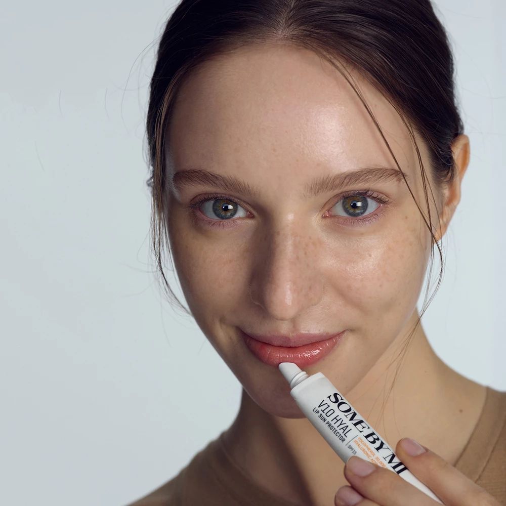 Frau hält Tube SOME BY MI V10 HYAL Lip Sun Protector. Produkt auf Lippen aufgetragen.