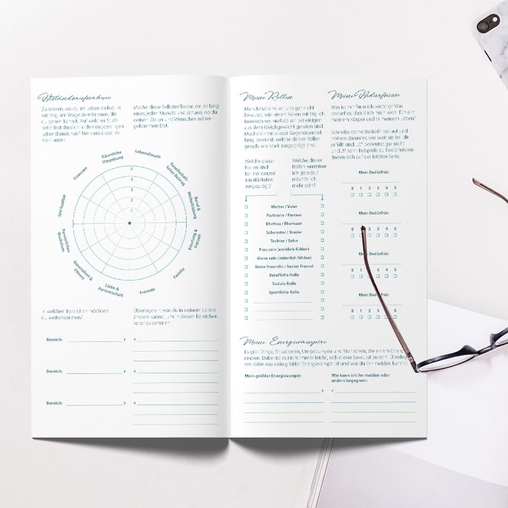 Geöffnetes blaues Tagebuch mit Text und Diagrammen. Brille liegt daneben. Aufschrift: create your life, daily journal.