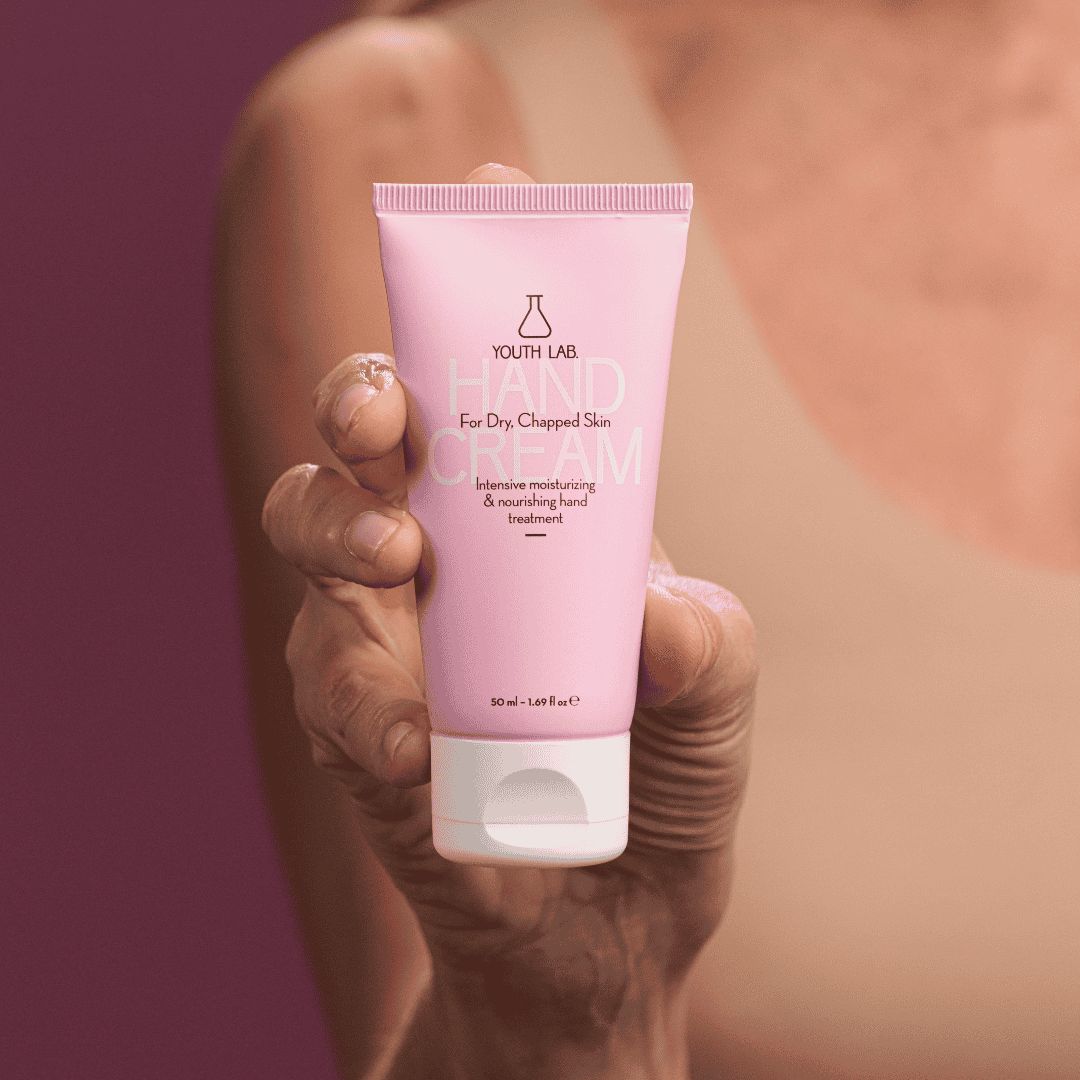 Rosa Tube mit weißem Verschluss. Aufschrift: YOUTH LAB Hand Cream For Dry, Chapped Skin. Hände halten die Tube.
