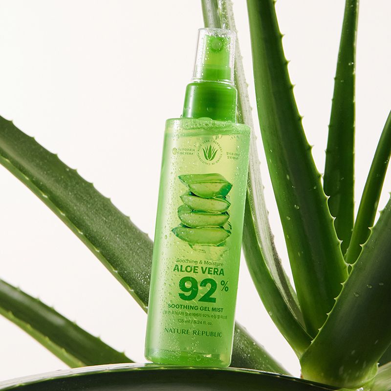 Grüne Sprühflasche mit Aloe Vera-Motiv, umgeben von Aloe-Pflanze. Text: Aloe Vera 92%. Marke: NATURE REPUBLIC. Transparente Flüssigkeit.