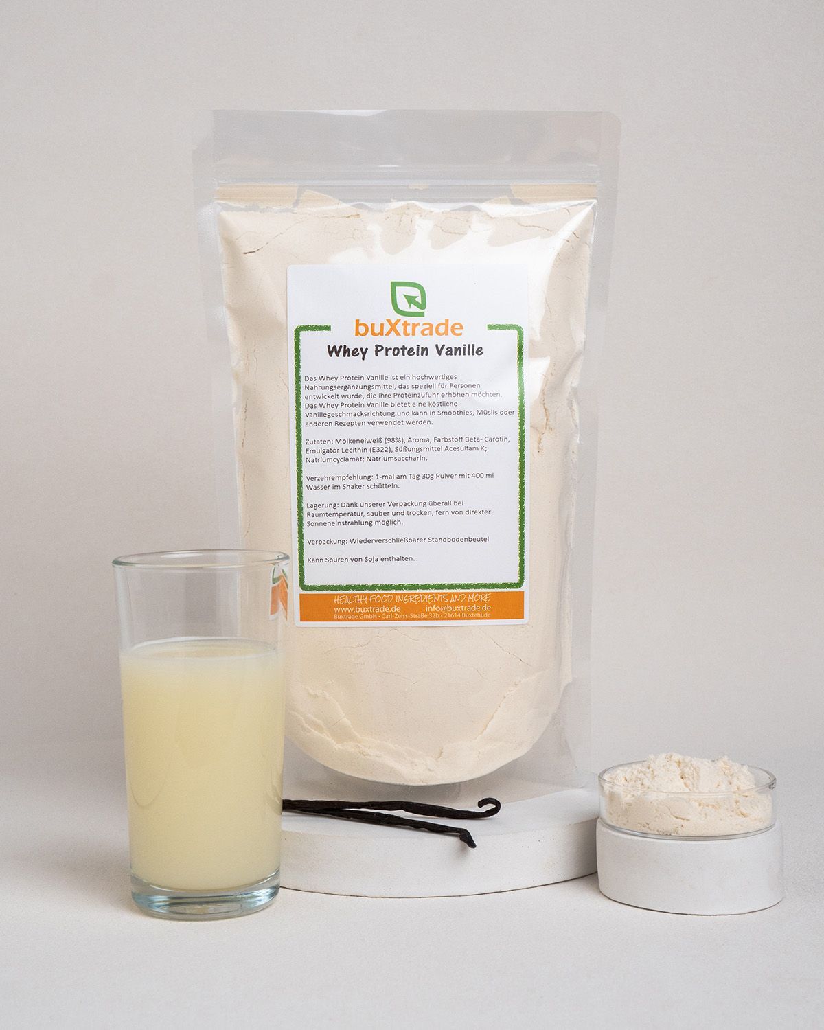 Transparente Tüte, Glas mit Flüssigkeit, Löffel, Vanilleschoten. Produktname: buXtrade Whey Protein Vanille. Text in Deutsch.