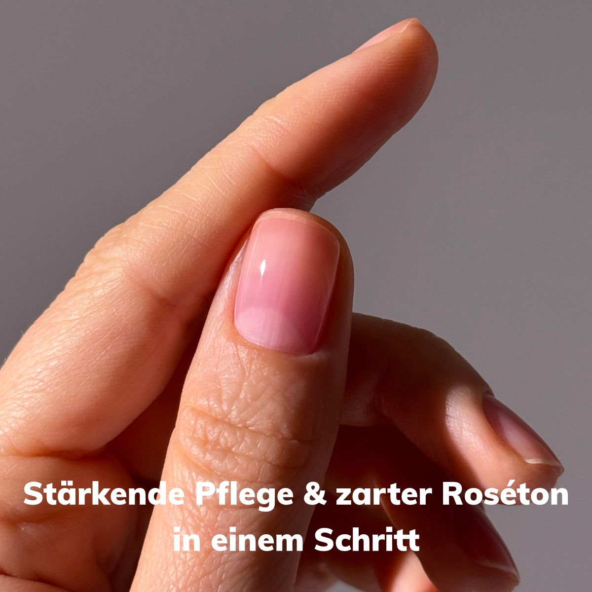 Eine Hand mit einem zartrosa, glänzenden Nagel. Text: Stärkende Pflege & zarter Roséton in einem Schritt.