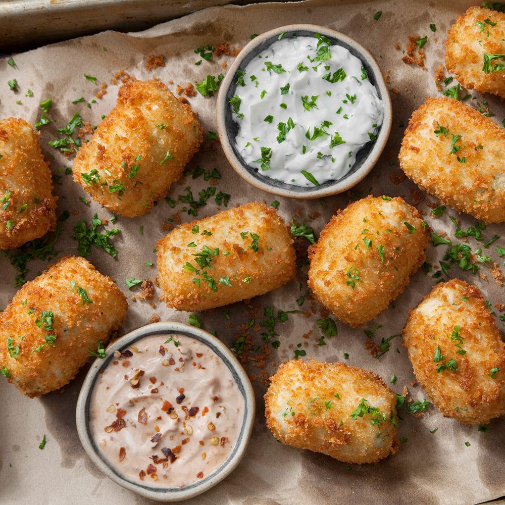 Gebratene Kroketten, zwei Schalen mit Sauce. Kroketten goldbraun, Sauce weiß und rosa. Petersilie als Garnitur.