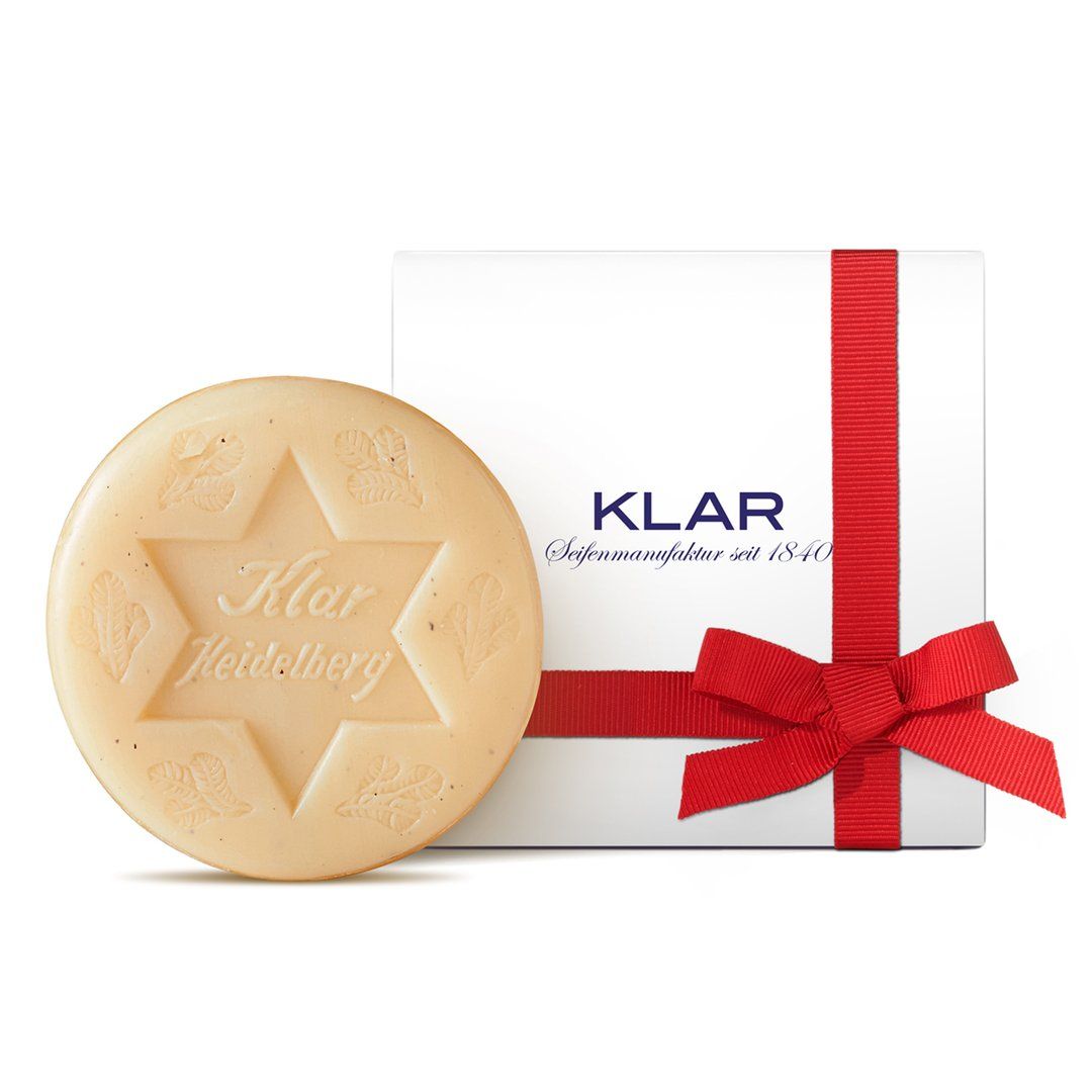 Runde Seife mit Sternmuster und Schriftzug. Weiße Geschenkbox mit roter Schleife. Klar-Logo.