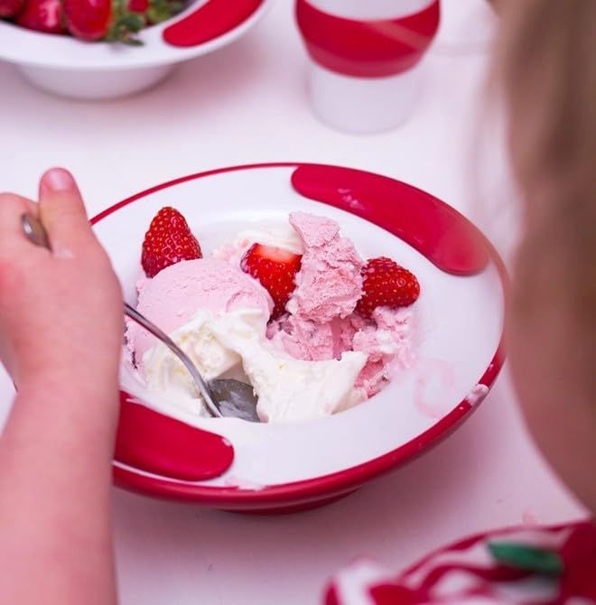 Kind isst Eis aus einer Schale. Rote Griffe, Erdbeeren und Eiscreme sichtbar.