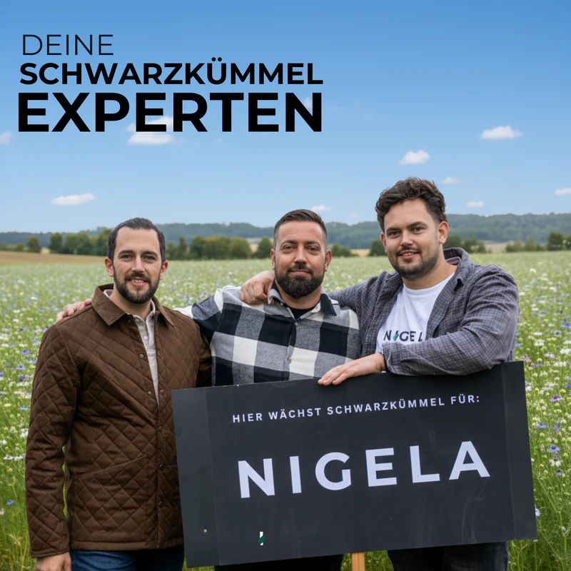 Drei Männer stehen auf einem Feld mit blauen Blüten. Sie halten ein Schild mit 'NIGELA'.
