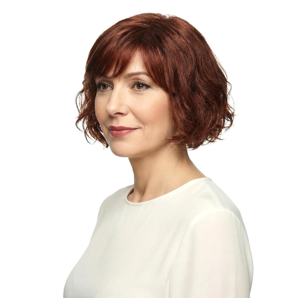 Frau mit rotbrauner, gewellter Perücke mit Pony. Blick zur Seite, vor weißem Hintergrund.