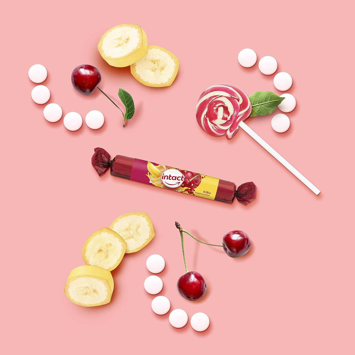 Traubenzucker-Rolle, Bananenscheiben, Kirschen, weiße Tabletten und ein Lutscher auf rosa Hintergrund. Auf der Rolle: intact Kirsch-Banane.