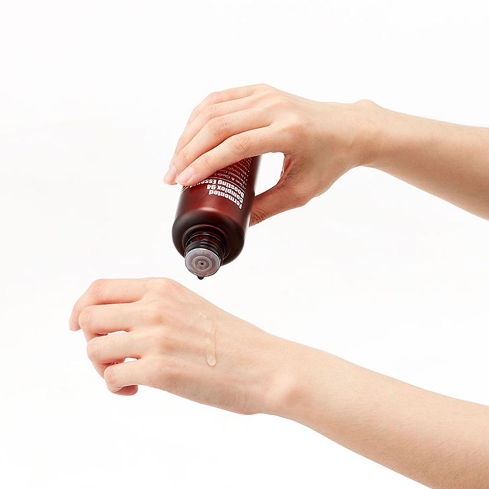 Hände halten eine braune Flasche. Flüssigkeit tropft auf die Handfläche. Flasche mit schwarzem Deckel.