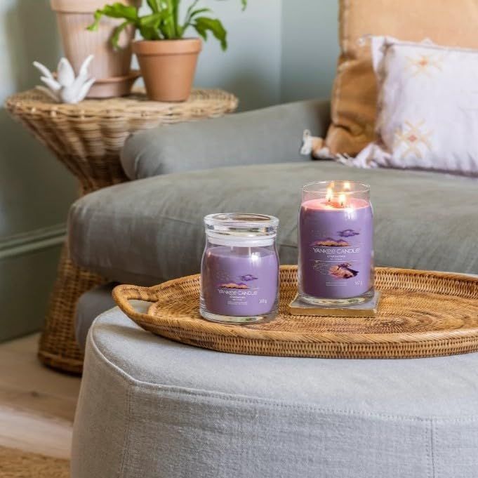 Zwei Kerzen auf einem Tablett. Eine brennt. Aufschrift: Yankee Candle. Umgebung: Sofa, Beistelltisch, Kissen.