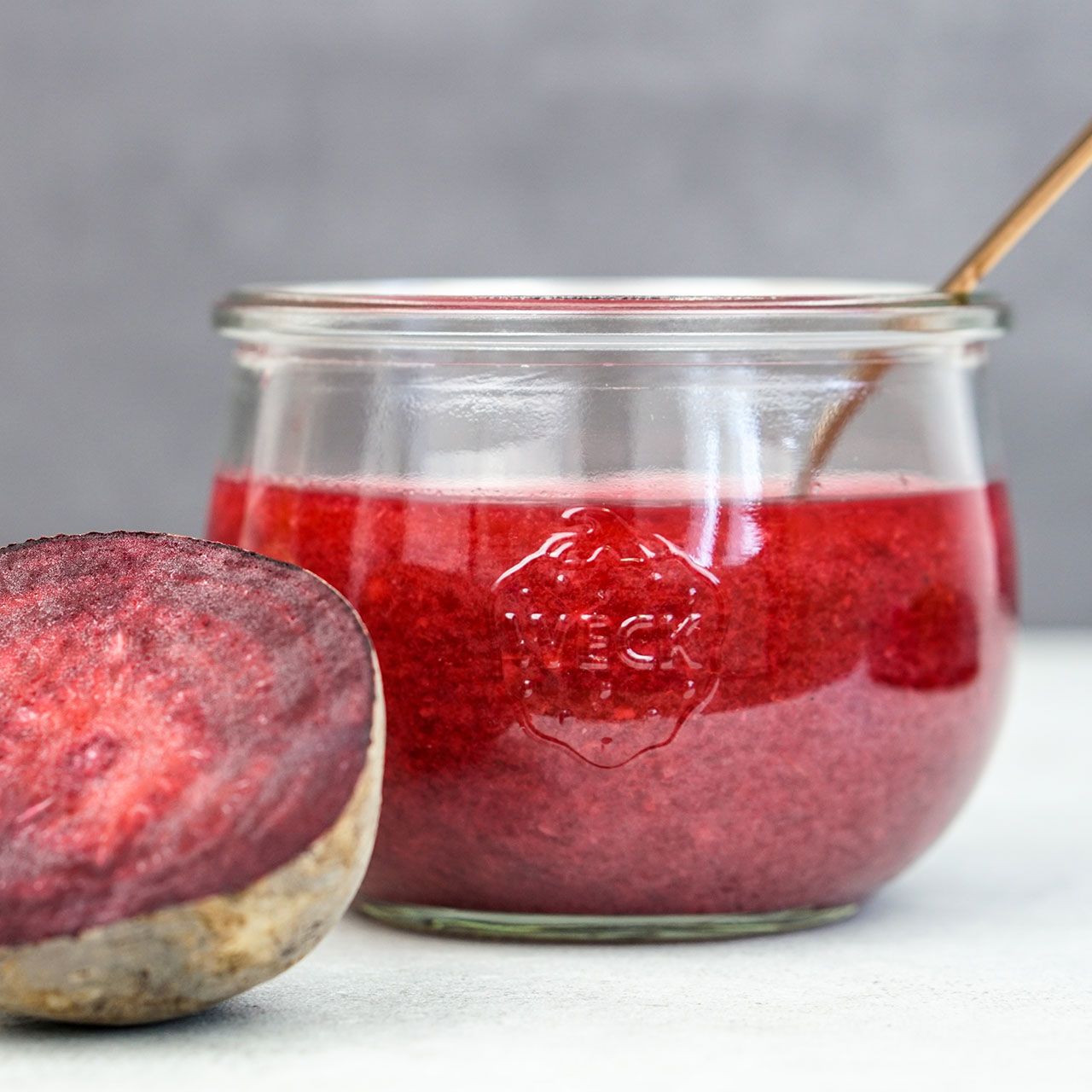 Glas mit roter Flüssigkeit und halber Rote Bete. Glas mit Weck-Logo. Auf weißem Untergrund.