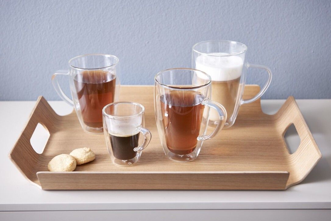 Holztablett mit Espressogläsern und Getränken. Verschiedene Größen und Füllungen. Auf weißem Tisch.