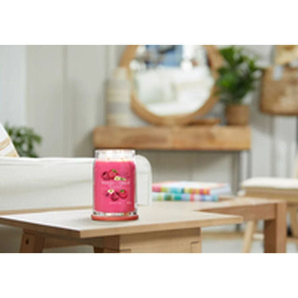 Rote Duftkerze auf einem Tisch. Im Hintergrund: Sofa, Spiegel und Dekoration. Aufschrift: Red Raspberry.