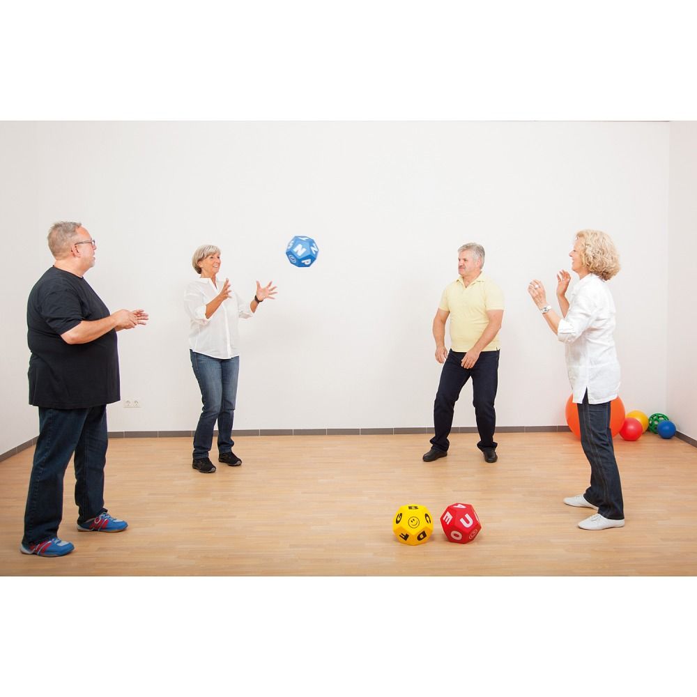 Mehrere Personen spielen mit Schaumstoffwürfeln mit Buchstaben. Gymnastikraum mit Holzboden.
