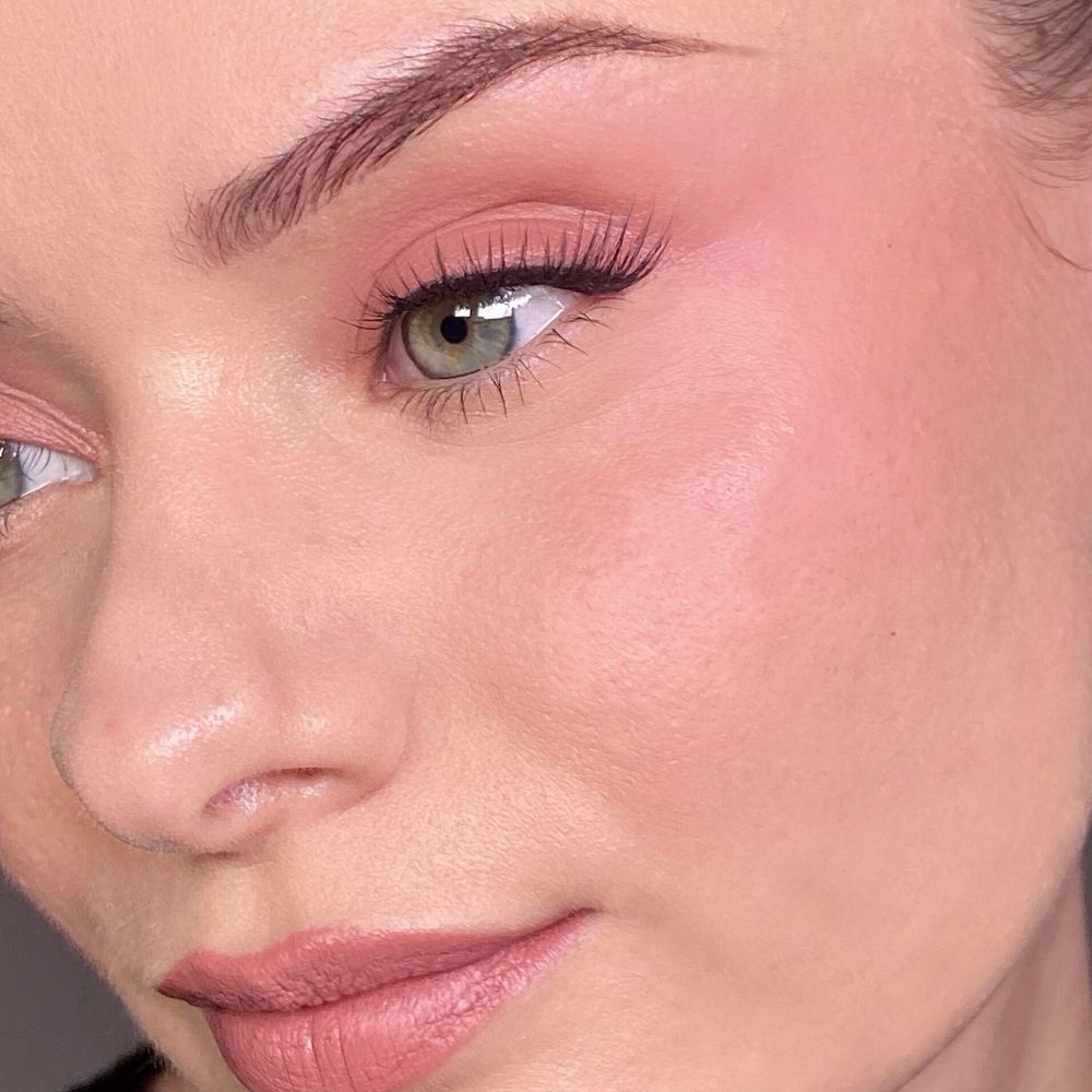 Nahaufnahme eines Gesichts mit rosa Make-up auf Augen und Wangen. Grüne Augen, falsche Wimpern.