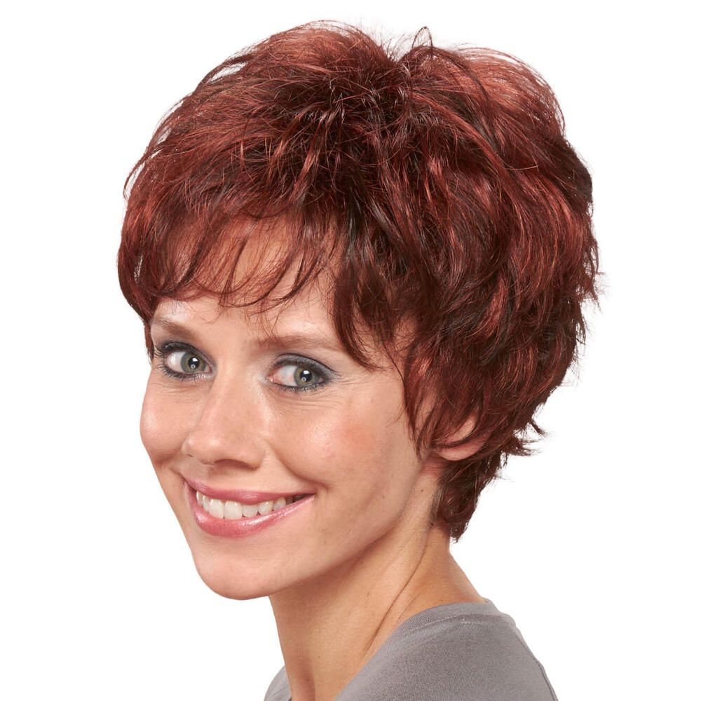 Kurzhaarperücke in Rotbraun. Die Frau lächelt. Blick nach rechts. Lockige Struktur. Pony. Graues Oberteil.