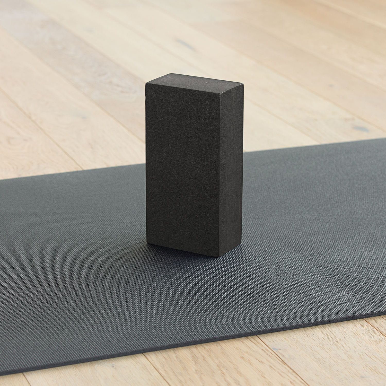 Schwarzer Yogaklotz steht auf einer Yogamatte. Rechteckige Form, aus Schaumstoff. Auf hellem Holzuntergrund.