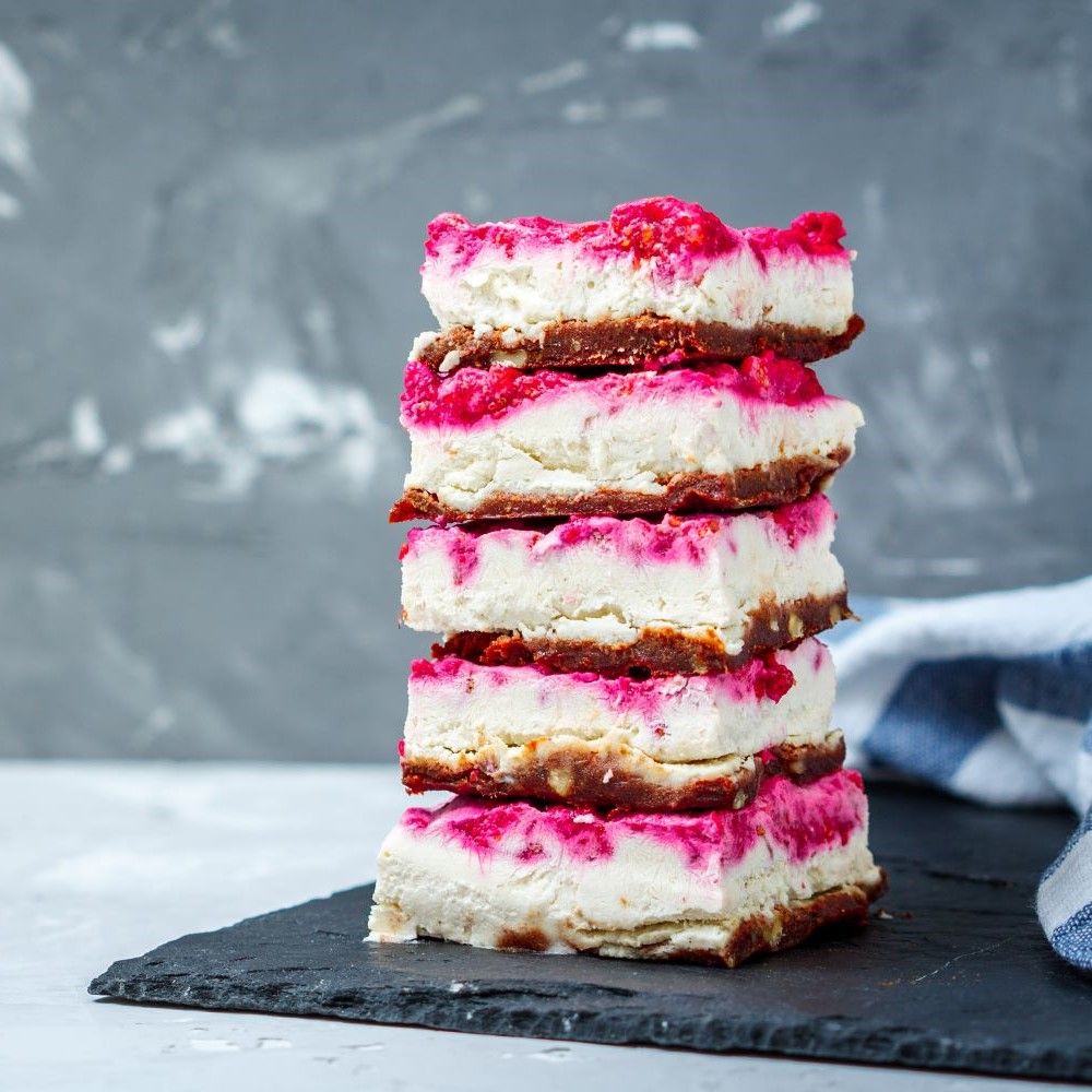 Gestapelte Kuchenstücke mit weißer Creme und roter Frucht. Auf schwarzem Brett.