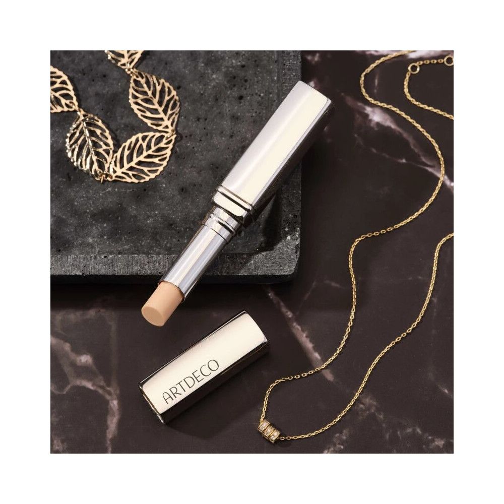 Ein silberner Lippenstift mit geöffneter Kappe und Produkt. Goldene Halsketten liegen auf einer dunklen Oberfläche.