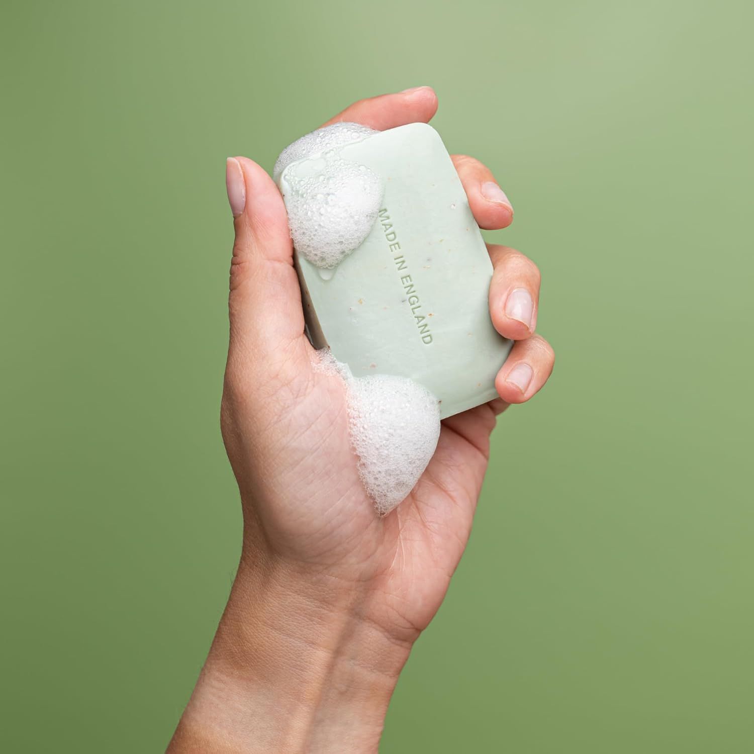 Hand hält grünes Seifenstück mit Schaum. Aufdruck "MADE IN ENGLAND".