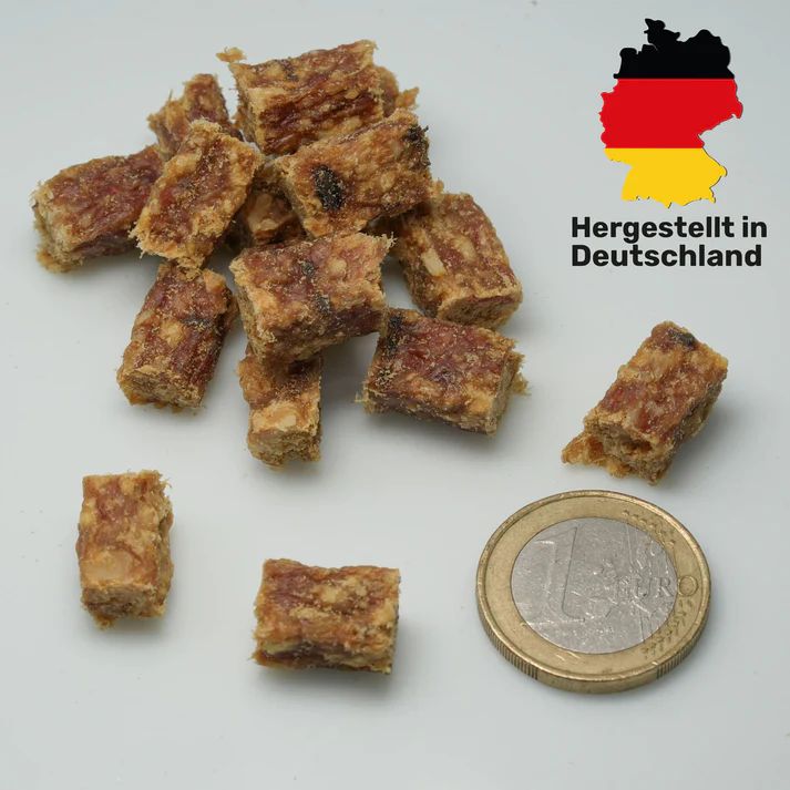 Hundesnacks in Würfelform. Neben den Snacks liegt eine 1-Euro-Münze. Aufschrift: Hergestellt in Deutschland. Flagge Deutschlands.