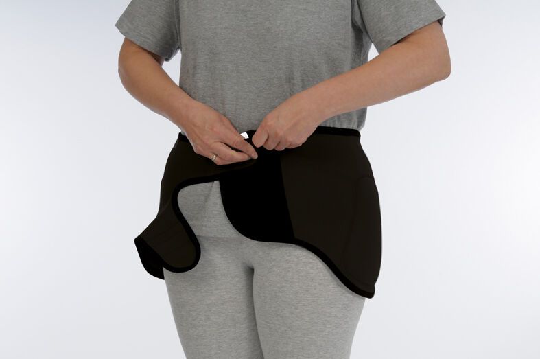 Schwarzer Hüftschutzgürtel, von Person getragen. Klettverschluss wird geschlossen.