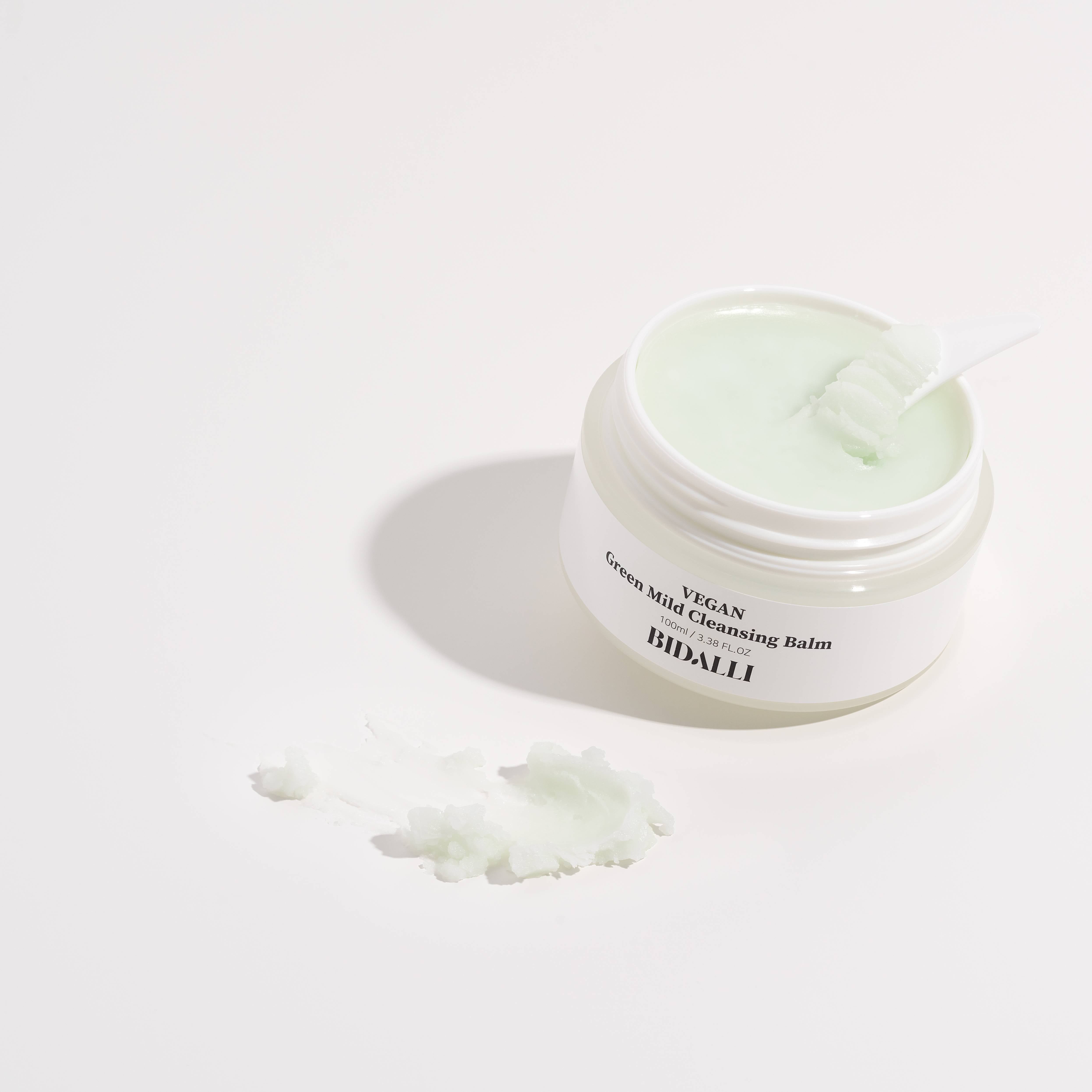 Offener Tiegel mit grünem Balsam und Spatel. Daneben ein Klecks Balsam. Auf dem Etikett steht: VEGAN Green Mild Cleansing Balm.