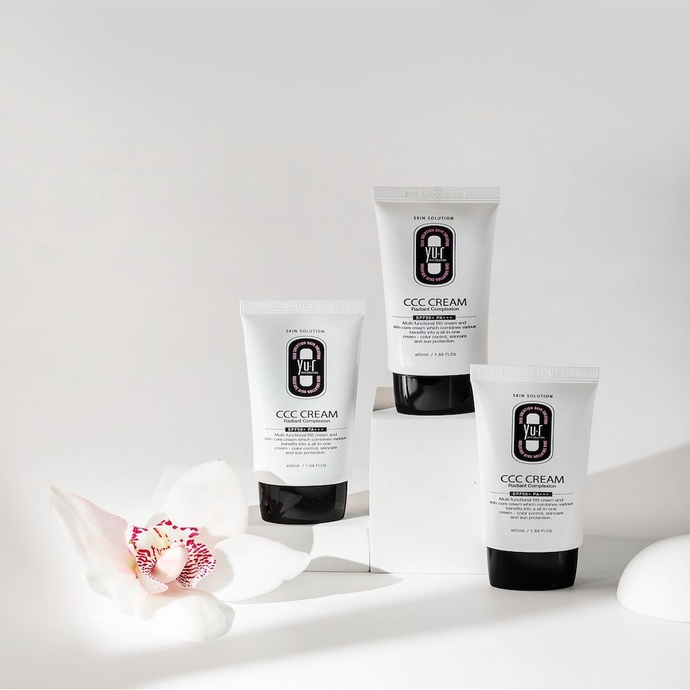Drei Yu.r CCC Cream Tuben auf Podesten. Schwarze Schrift. 50ml/1.69 FL.OZ. Mit Orchidee.