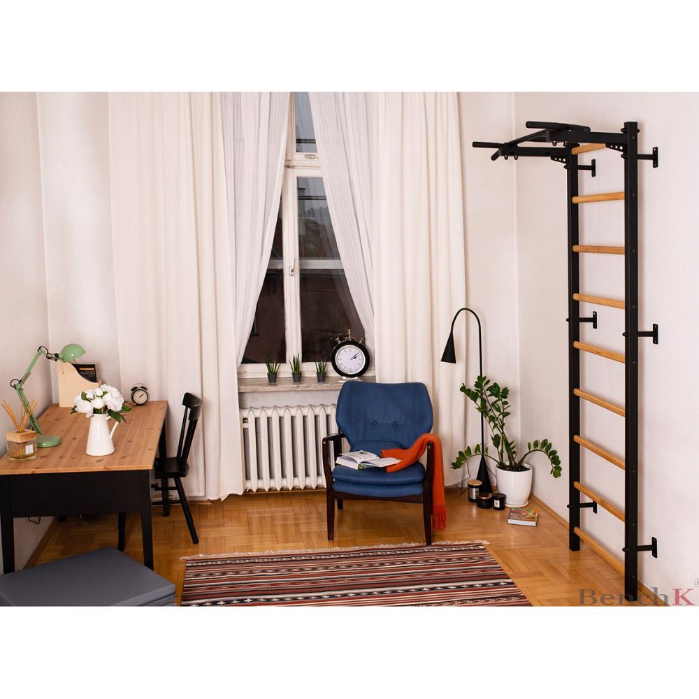 Sprossenwand mit Klimmzugstange, in Wohnraum. Schwarzer Rahmen, Holzsprossen. In der Nähe eines Fensters.