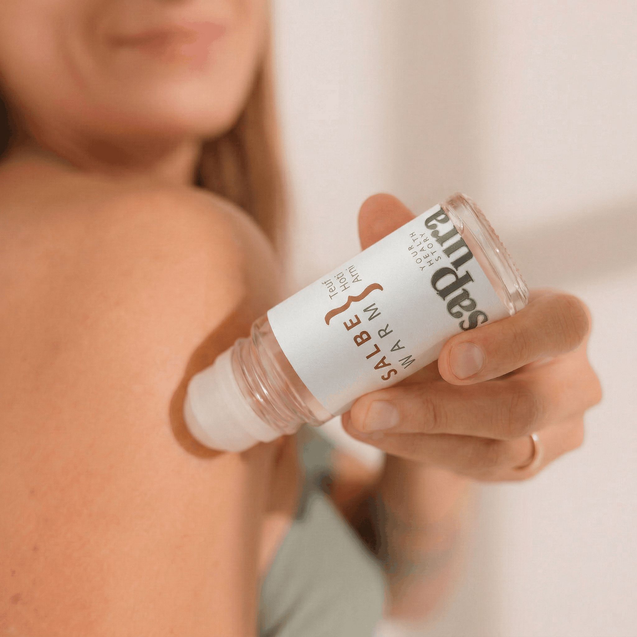 Eine Hand hält eine sapura® Roll-On Flasche mit Wärmesalbe und rollt sie auf die Schulter.
