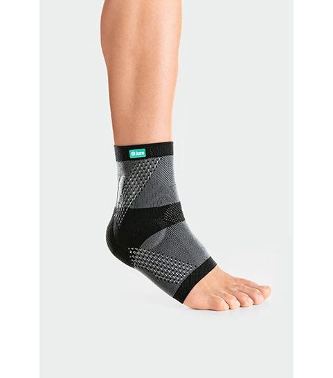 Knöchelbandage JuzoFlex Malleo Xtra am Fuß. Grau-schwarzes Material, offene Ferse, Logo. Angedeutete Struktur.