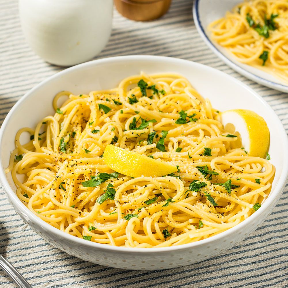 Schüssel mit Spaghetti, Kräutern und Zitronenscheibe. Auf gestreiftem Untergrund.