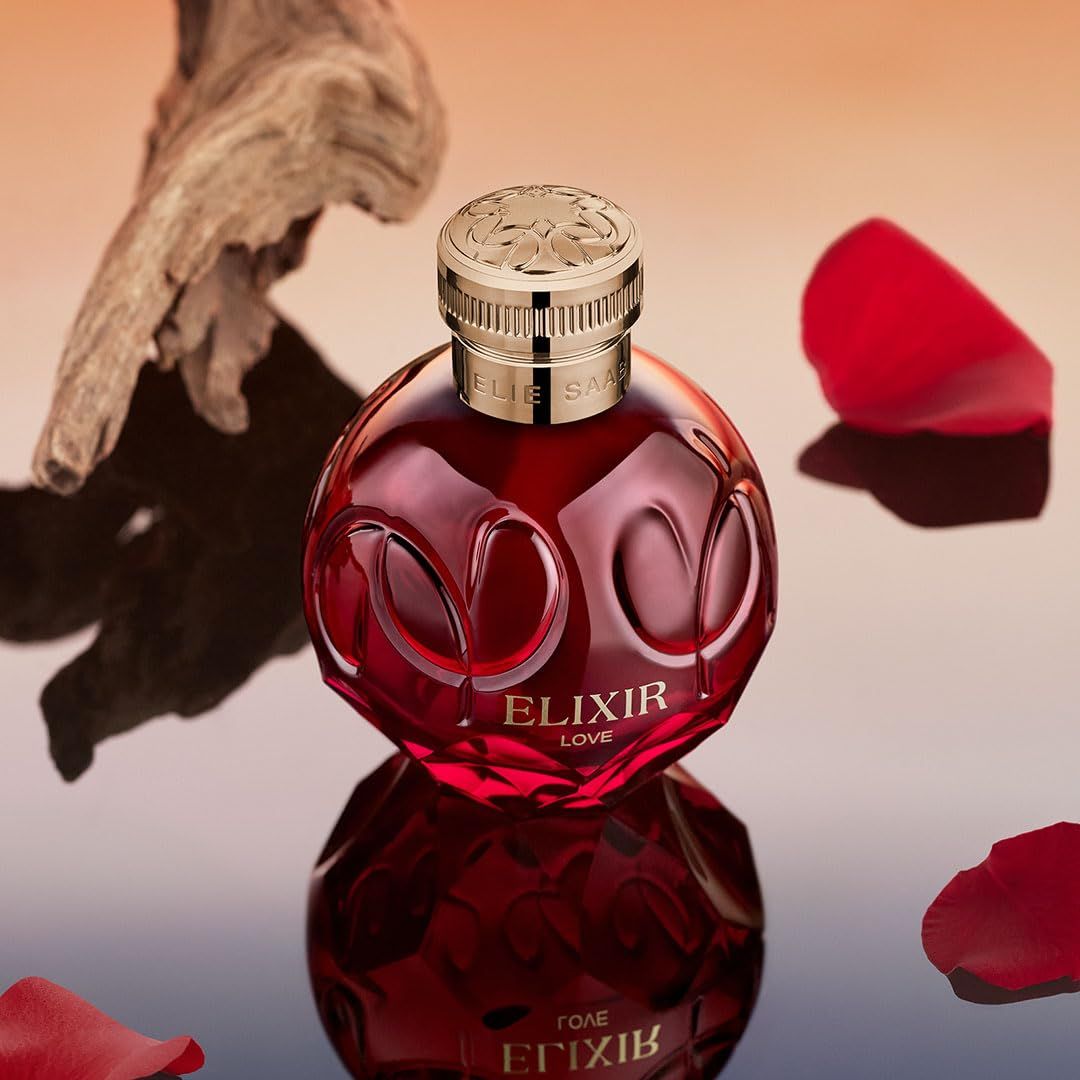 Roter Flakon mit goldfarbenem Deckel. Aufschrift: ELIXIR LOVE. Flakon auf glänzender Oberfläche mit Holzstück und Blütenblatt.