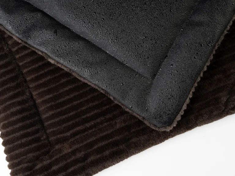 Gefütterte Liegedecke, braune Oberseite, schwarze Unterseite. Detailansicht der Materialien.