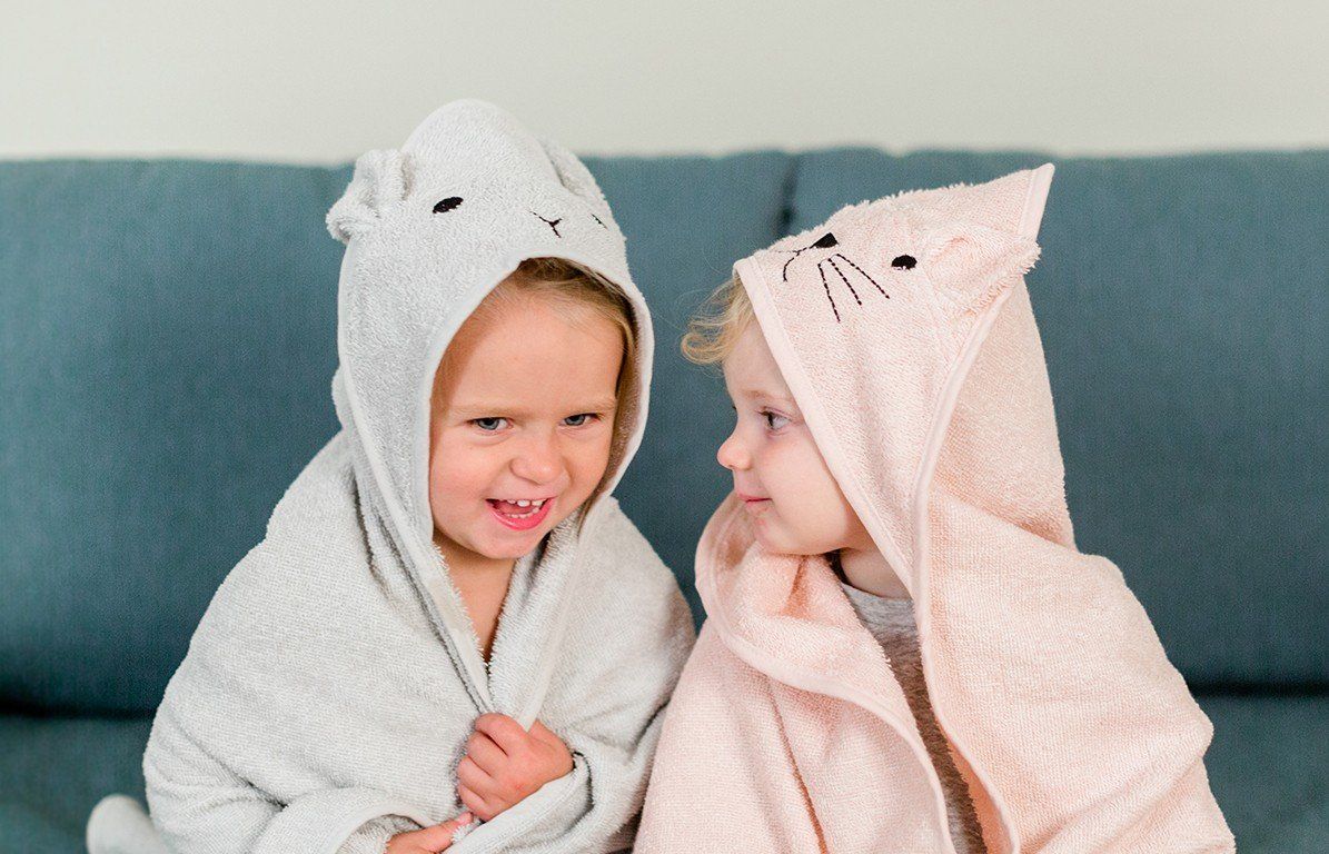 Zwei Kinder in Kapuzenhandtüchern. Eines grau mit Hasenohren, das andere rosa.