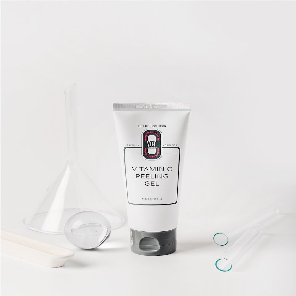 Weiße Tube mit grauer Kappe und Aufschrift Vitamin C Peeling Gel. Laborutensilien im Hintergrund.