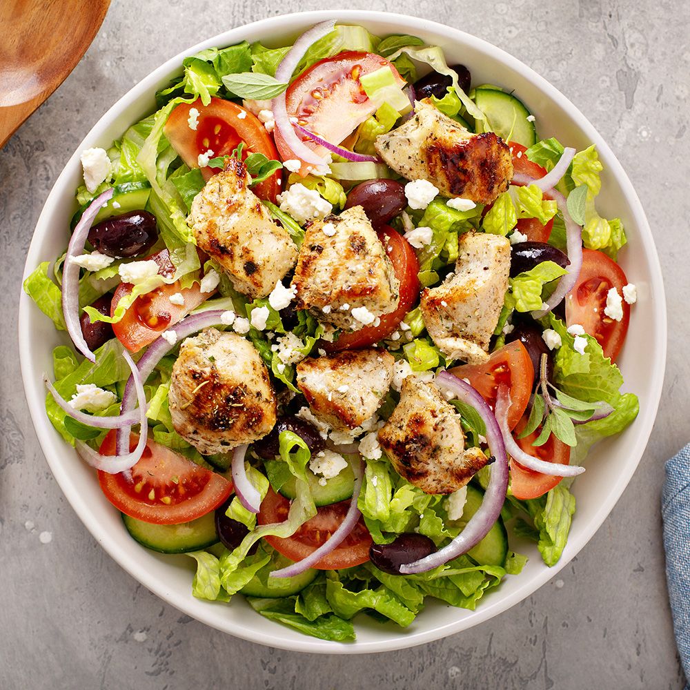 Salatschüssel mit Salat, Tomaten, Hähnchen, Zwiebeln, Oliven und Feta. Draufsicht. Helles Ambiente.