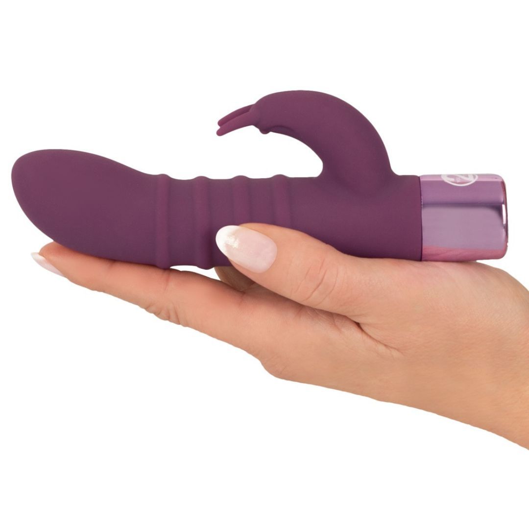 Lila Vibrator in einer Hand gehalten. Mit geriffelter Oberfläche und gebogener Spitze. Silberfarbener Sockel.