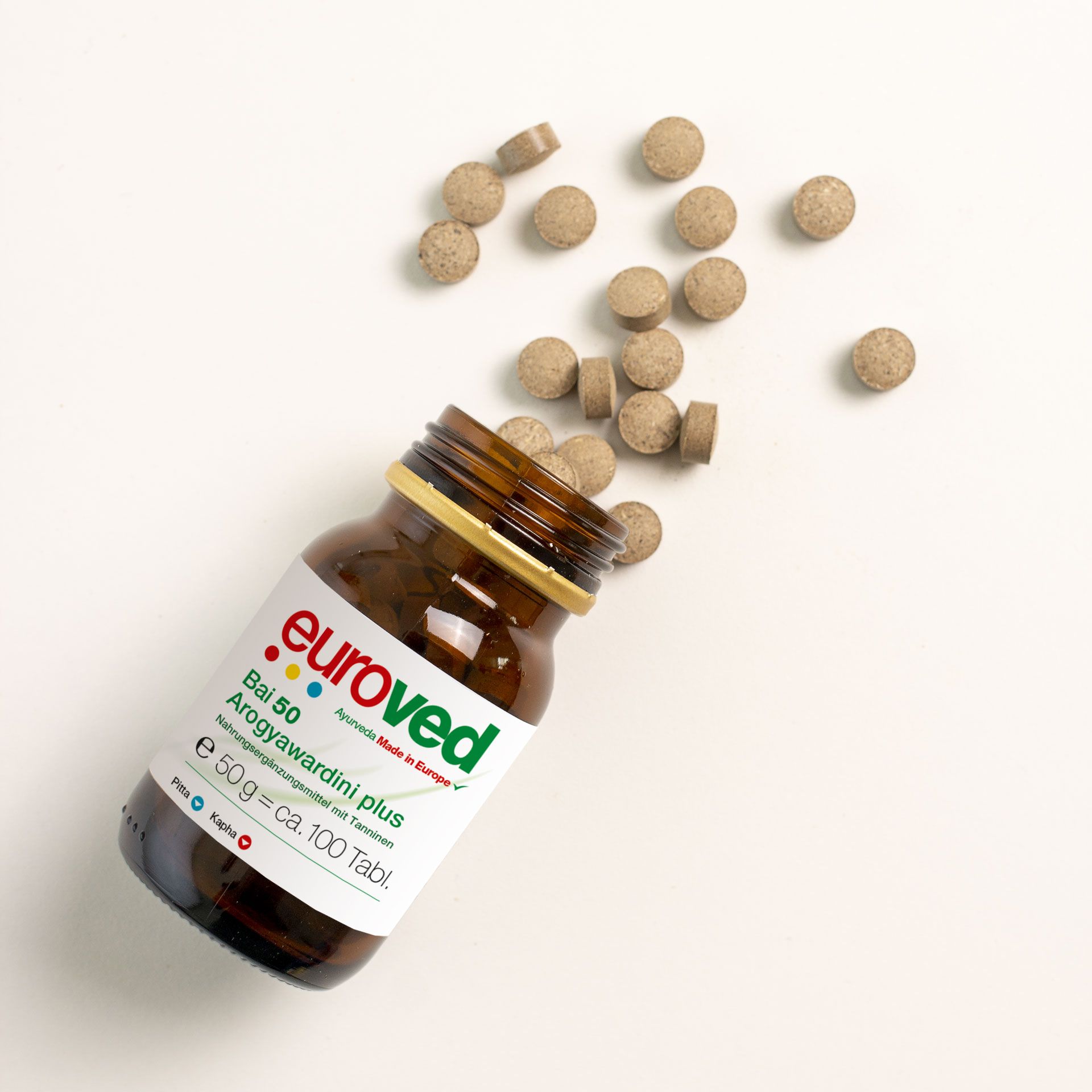 Braune Tabletten neben einer braunen Glasflasche. Auf der Flasche steht "euroved Bai 50 Arogyawardini plus".