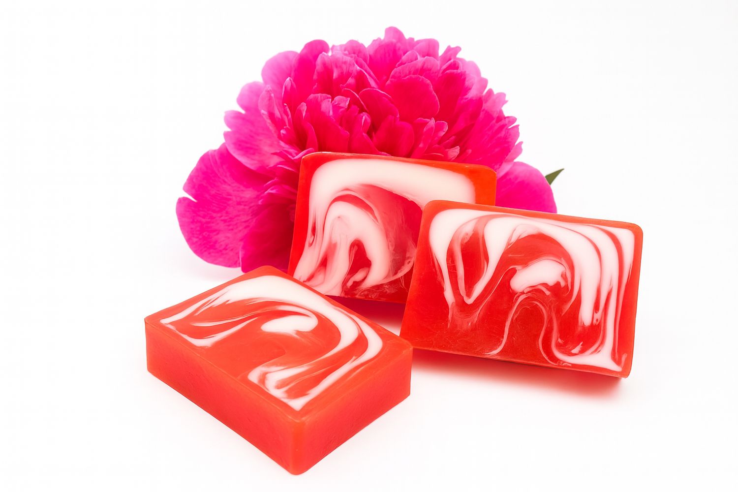 Drei rechteckige Seifenstücke mit roter und weißer Marmorierung. Dahinter eine pinke Pfingstrose.