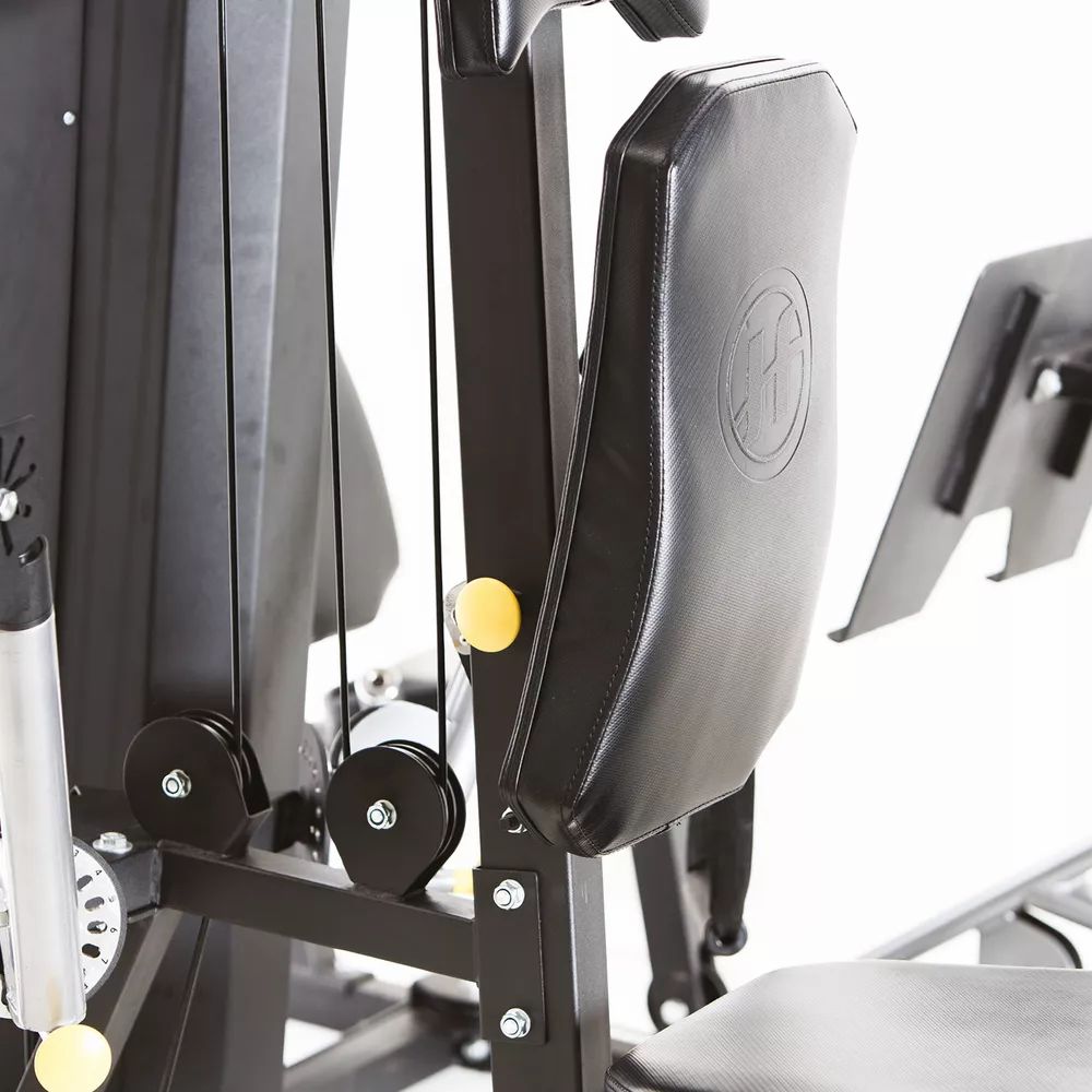 Detailansicht der Fitnessstation. Schwarze Polsterung mit Logo. Umlenkrollen und Seilzüge. Gelbe Verstellknöpfe. Horizon Fitness Torus 5.