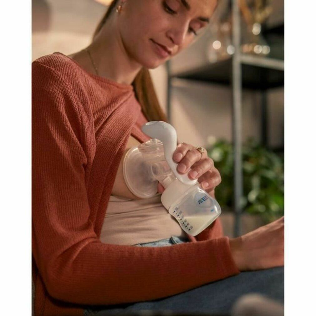 Frau benutzt eine PHILIPS AVENT manuelle Milchpumpe. Sie sitzt und hält die Pumpe an ihrer Brust.