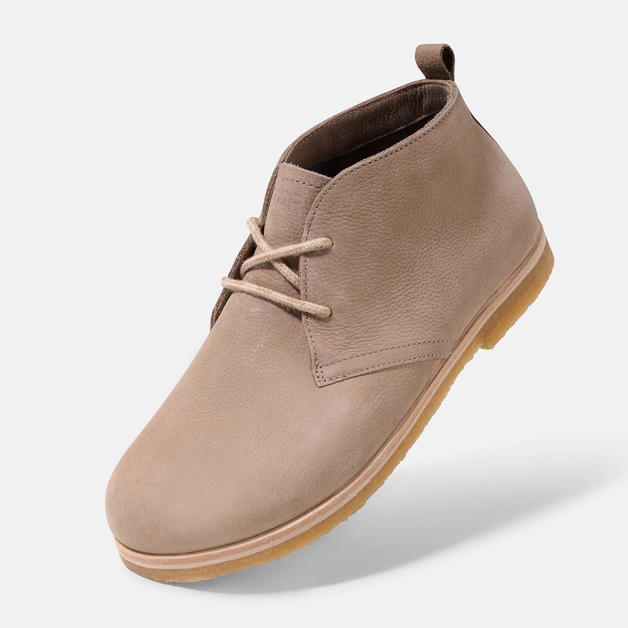 Beige Stiefelette mit Schnürsenkeln. Hellbraune Sohle. Obermaterial aus Leder. Auf hellem Hintergrund, leicht schräg.