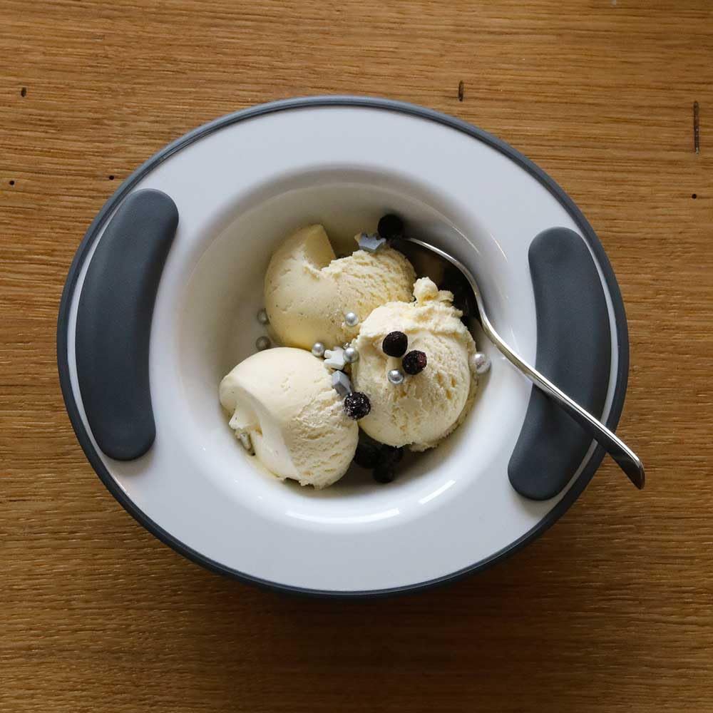 Weiße Schale mit Eiscreme, silbernen Streuseln und einer silbernen Gabel. Graue Griffe an der Schale.