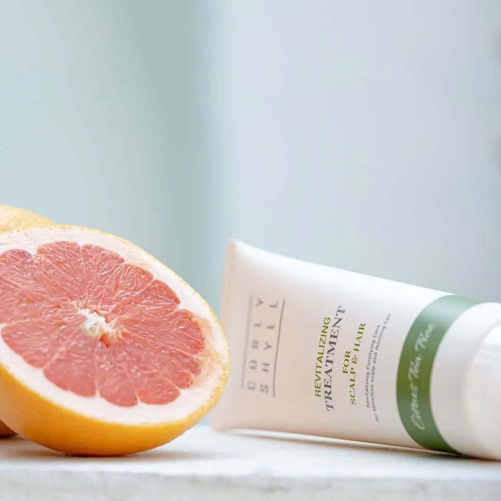 Beige Tube mit grünem Streifen. Text: CURLY SHYLL, Revitalizing Treatment for Scalp & Hair. Daneben eine Grapefruit.